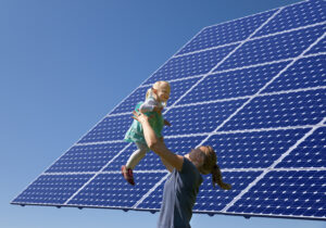 Woman lifting little girl up, in front of solar panel.