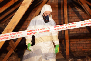 A man wearing protective clothing while clearing asbestos from an attic.