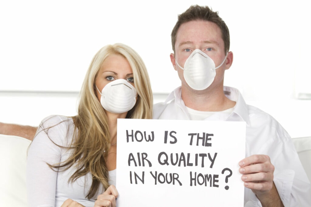 young couple cuddling on their couch with breathing masks on and a sign that says 