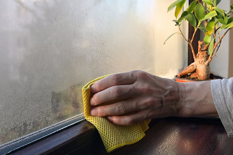 How Can You Manage Your Home’s Humidity. Window with condensation being wiped with a rag.